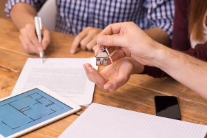 Happy young couple getting keys of their new house. Close up of female hand receiving keys from house broker. Closeup of the hand of a real estate agent who give the house keys to a woman while her boyfriend signing a contract.